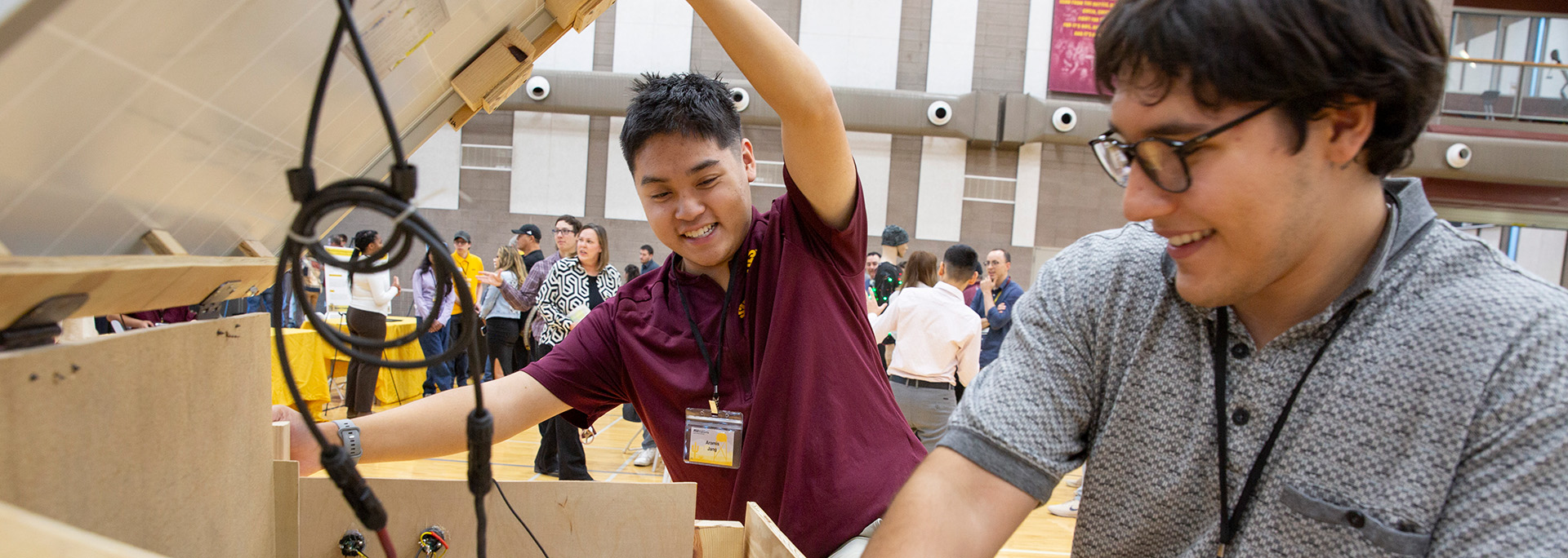 Two engineering students lift up a wooden box to fix their demo project at the Innovation Showcase